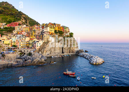 Panorama von Manarola, Cinque Terre, La Spezia. Farbenfrohe Gebäude in der Nähe der ligurischen Meer. Blick auf die Boote in der Marina mit blauen Wasser bei Sonnenuntergang günstig Stockfoto