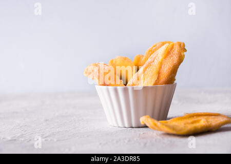 Entwässert und getrocknet mango Chips in Weiß Schüssel auf konkrete hellen Hintergrund. Close Up. Stockfoto
