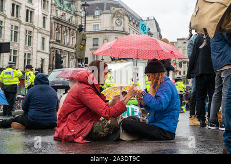 7 Oct 2019 - London, UK. Einen Demonstranten teilen sich einen Regenschirm beim Blockieren die Straße während Aussterben Rebellion Klima Protest in London. Stockfoto