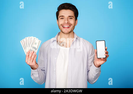 Lächelnd Mann zeigt leere Seite Telefon holding Bündel Geld Stockfoto