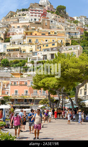 POSITANO, ITALIEN - AUGUST 2019: die Menschen an der Küste von Positano schlendert. Es ist von bunten Gebäude am steilen Hang übersehen. Stockfoto