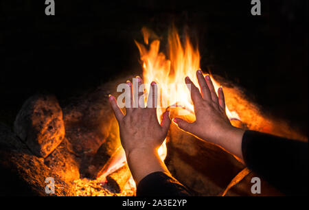 Lodernden Lagerfeuer und alte einsame Frau im Detail über Nacht schwarzen Hintergrund. Weibliche Hände mit den Fingern über warmen Feuer mit orange Brennen Flammen gespreizt. Stockfoto