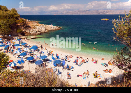 Urlauber Sonnenbaden auf Liegen und Liegestühlen unter Sonnenschirmen am Strand am Griechischen Ferienort Kassiopi auf der Insel Korfu in Griechenland Stockfoto