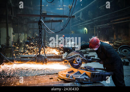 Männliche Arbeiter tragen spezielle Schutzhandschuhe, Schneiden von Metall mit großen elektrische Kaffeemühle, orange Funken während der Arbeit mit Stahl im Werk fliegen Stockfoto