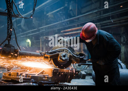 Männliche Arbeiter tragen spezielle Schutzhandschuhe, Schneiden von Metall mit großen elektrische Kaffeemühle, orange Funken während der Arbeit mit Stahl im Werk fliegen Stockfoto