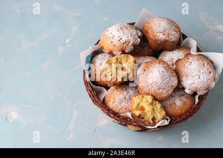 Hausgemachte Muffins mit getrockneten Aprikosen, bestreut mit Puderzucker in einem Weidenkorb auf hellblauem Hintergrund, horizontale Ausrichtung, Ansicht von oben Stockfoto