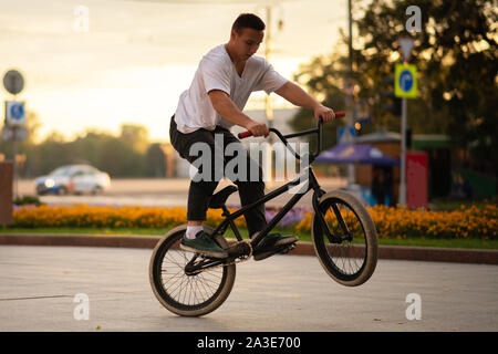 Der Mann führt ein BMX Stunt beim Stehen auf dem Hinterrad. Stockfoto