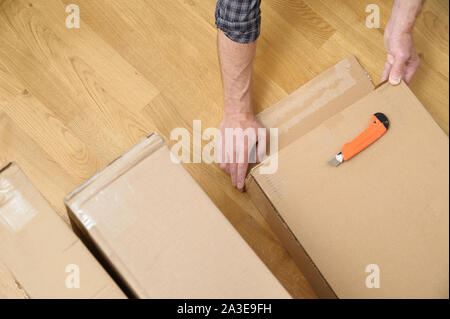 Ein Mann wird das Auspacken der Kartons. Es öffnet die Seite des Pakets. Stockfoto