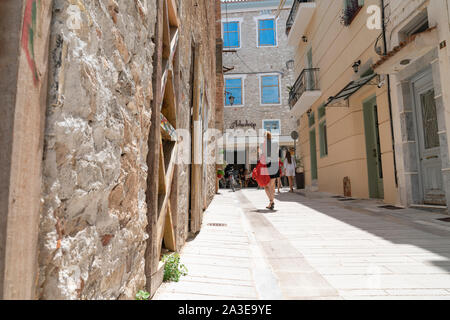 Nafplio Griechenland - 18 Juli 2019; Frauen, eine tragende rote Einkaufstasche wandern in schmale Gasse in Richtung Cafe am Ende in kleinen griechischen Dorf von Nafplio. Stockfoto