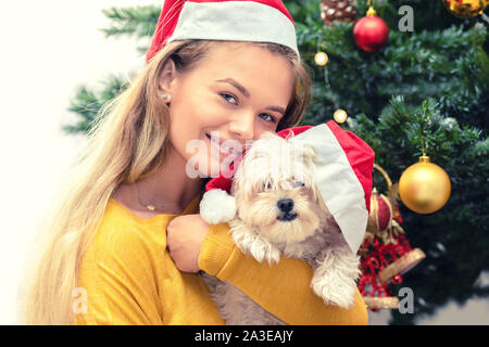 Glückliche Frau tragen Santa Hut mit kleiner Hund warten auf das Neue Jahr Stockfoto