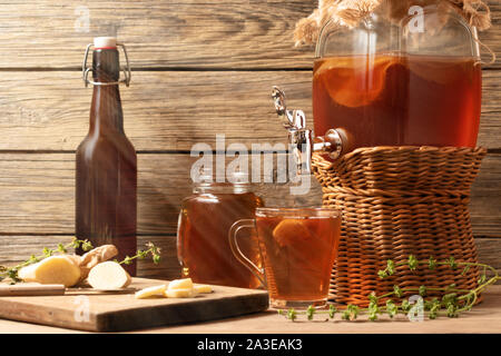 Frische hausgemachte Kombucha fermentierter Tee trinken in Glas mit Hahn und in Dosen - Tassen und Becher auf Holz- Hintergrund. Stockfoto