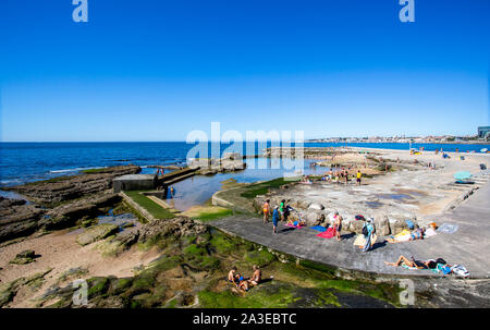 Menschen die Sonne genießen und den Atlantischen Ozean, die um einen Pool auf der auf den Felsen der Strand von Tamariz, in Estoril, Portugal gebaut Stockfoto