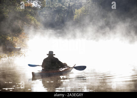 Kajakfahrer paddeln an einem kalten Herbstmorgen im Algonquin Park Ontario WP durch Nebel auf einem Fluss Stockfoto