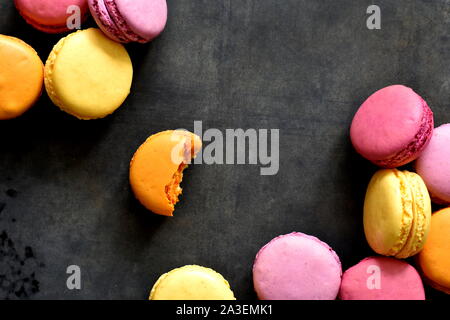 Fröhliche Fröhliche bunte Kekse Hintergrund. Zerstreut, pink, gelb und orange Französische Makronen oder Cookies auf dunkelgrau Metallwanne Hintergrund. Stockfoto