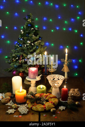 Weihnachtsbaum, brennende Kerzen im Kerzenständer, eine Runde rituelle Brot, Lebkuchen Kekse, Walnüsse auf dem hölzernen Tisch sind. Stockfoto