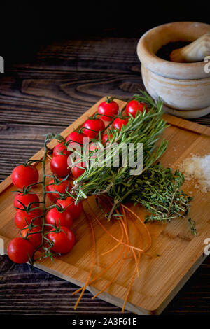 Frische Tomaten cherry, grüne Blätter Rosmarin Kräuter, Salz und unvorbereitet Spaghetti auf Holzbrett über Ansicht, Hintergrund restaurant Dekoration Stockfoto