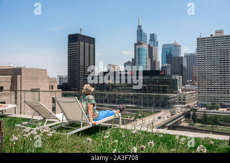 Downtown Philadelphia, Rückansicht eines Solo reife Frau am Philadelphia Skyline, sitzend auf einer Dachterrasse mit Liegestühlen, Pennsylvania, PA, USA Stockfoto