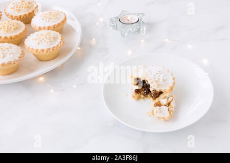 Mince Pies auf Platten mit Kerzen und Lichterketten auf weißem Hintergrund mit kopieren. Stockfoto