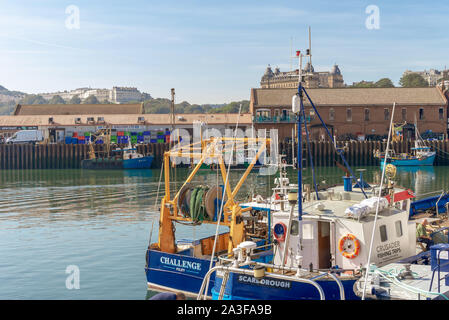 Der Hafen von Scarborough. Zwei Fischerboote vertäut an einen Kai mit einem langen Wharf im Hintergrund. Hotels und Hügel sind in der Entfernung. Stockfoto