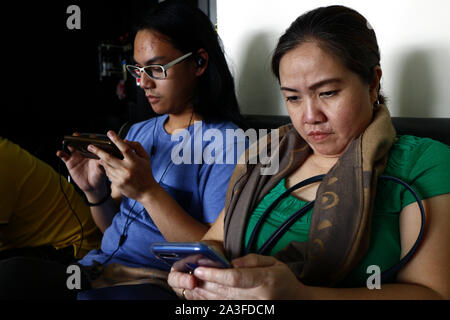 Foto von Erwachsenen schöne asiatische Frau und hübscher junger Erwachsener verwenden, Smartphone, während im Wartebereich Stockfoto