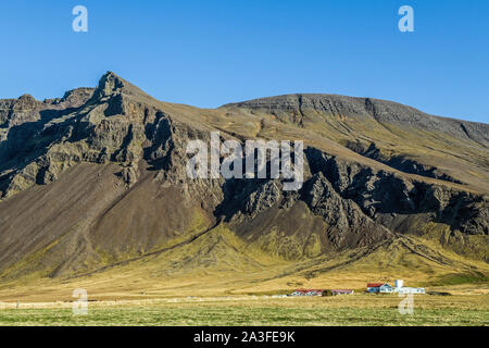 Celandic Farm in der Nähe von Grundarhverti im Nordwesten von Reykjavic, unterhalb der vulkanischen Felsenberge, einer typischen isländischen Landschaft. Stockfoto