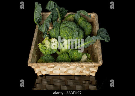 Menge ganze Frische grüne Brokkoli in geflochtenen Korb auf schwarzem Glas isoliert Stockfoto