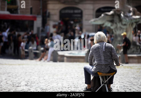 Frau, die auf einem Künstlerhocker sitzt und einen Blick auf eine Baroque Fountain Plein Luft auf einer Piazza in Rom malt. Stockfoto