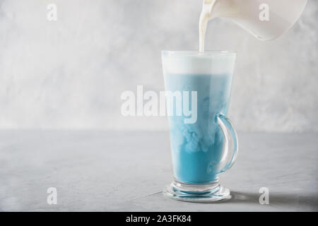 Blau Matcha Tee und Gießen Milch in Latte Glas auf grau Tabelle. Platz für Text. Close Up. Horizontale Ausrichtung. Stockfoto