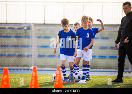 Jungen Training Fußball auf Pitch Hexe Jugend Coach. Gruppe von Jungen Schulpflichtigen Jungen auf Training mit Jugend Coach. Kinder im Blauen Jersey Schulen & Stockfoto