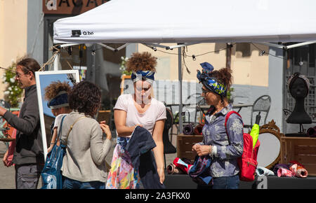 Zwei Frauen diskutieren über den Kauf eines Krawatte Turban an einem Straßenstall in Italien. Ihnen hilft der Stall Holder mit den von ihnen gewählten Hüten. Stockfoto