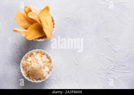 Entwässert und getrocknet Mango und Kokos Chips in Weiß Schüssel auf konkrete hellen Hintergrund. Blick von oben. Stockfoto