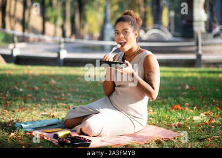 Dunkelhäutige Frau mit Tattoo auf dem Arm kleines Picknick geniessen. Stockfoto
