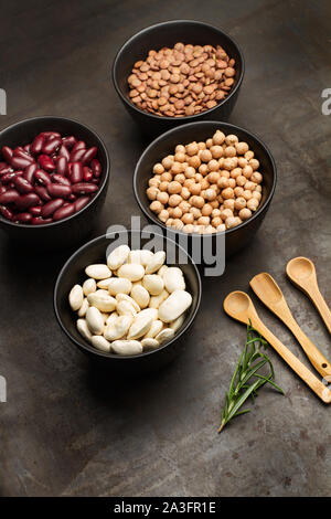 Bohnen, Linsen und Kichererbsen in schwarzem Schälchen mit Holzlöffel auf einem rostigen Tabelle Stockfoto