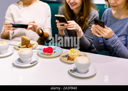 Frauen Freunde auf der Suche nach Kuchen im Cafe, die Fotos auf den Smartphones. Freunde Fotos schauen und Lachen, Cafe, Frauen, fun, Genießen Stockfoto