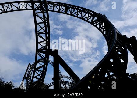 Niedriger Blick, der durch die sich schlängelnden schwarzen Stahlschienen der Achterbahn The Smiler im Freizeitpark Alton Towers unter einem bewölkten blauen Himmel aufsteigt, Stafford Stockfoto