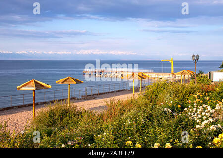 Ansicht des Issyk-Kul See, ein Strand mit Blick auf Issyk-Kul See, ein Strand mit Sonnenschirmen und Rasen mit Blumen und Berge am Horizont Stockfoto