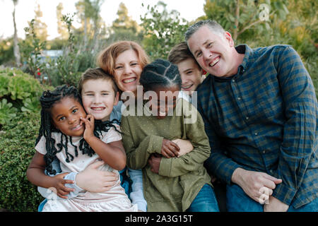 Freudige mixed-race Familie mit vier Kindern umarmen im Freien Stockfoto