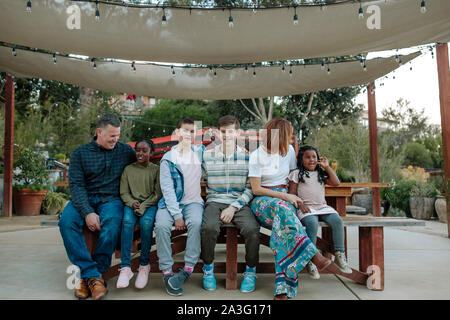 Lächelnd mutliracial Familie sitzt auf der Bank unter dem Sonnenschirm auf der Gärtnerei Stockfoto