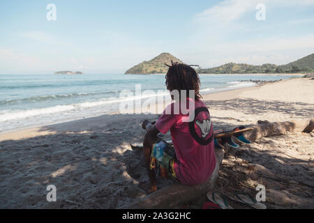 Ansicht der Rückseite des Mann mit Surfbrett am Ufer sitzen Stockfoto