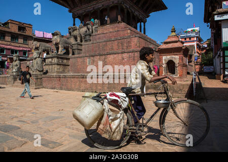 Ein Junge geht ein Fahrrad durch eine Plaza in Bhaktapur, Kathmandu, Nepal Stockfoto