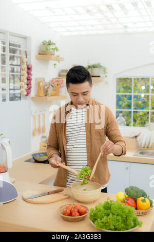 Lächelnden jungen Mann, Gemüse Salat in der Küche zu Hause. Stockfoto