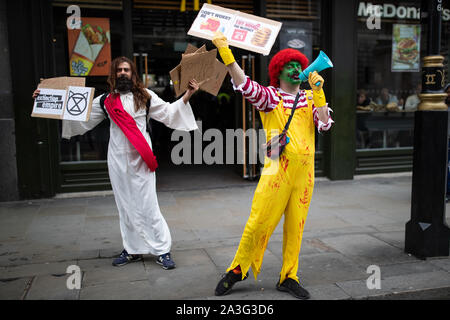 Die Demonstranten gekleidet, wie Jesus und Ronald McDonald außerhalb ein McDonald's Restaurant in der Nähe des Trafalgar Square, London, während ein Aussterben Rebellion (XR) Klimawandel protestieren. Stockfoto