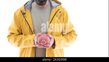 Mittelteil der Mann im gelben Regenmantel Holding rosa Sparschwein in beiden Händen Stockfoto