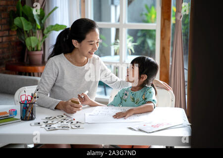 Glückliche Mutter ihre Tochter die grundlegenden Lehren zu Hause zu lesen und zu schreiben. Kleinkind kindergarten Student Stockfoto