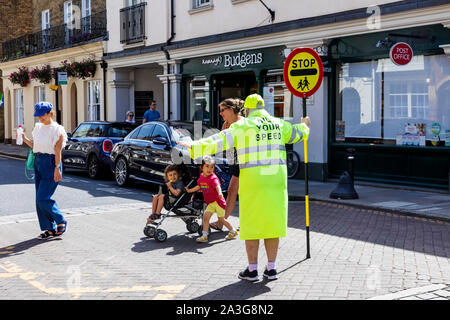 England, Berkshire, Eton, Eton High Street, Lollipop Lady Holding Stoppschild mit Fußgänger die Straße überqueren Stockfoto