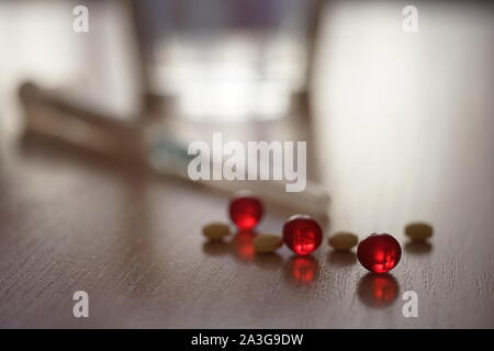 Pillen und rote Vitamine. Spritze und Wasser Glas in verschwommenen Hintergrund. Behandlung und Verwertung, Diät oder Drogenabhängigkeit. Stockfoto