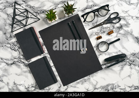 Blatt schwarzes Papier, Bleistifte, Brille, Lupe, Schere, Hefter, zwei Ordner, Bügeleisen Dreieck Abbildung, schöne grüne Pflanzen in den Töpfen und Büroklammern Stockfoto