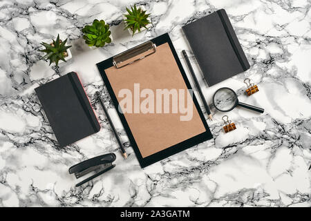 Schwarz, Klemmbrett mit braunem Papier, Bleistifte, Lupe, Hefter, zwei Ordner, Büroklammern und grünen Pflanzen in den Töpfen auf Marmor tisch mit kopieren. Stockfoto