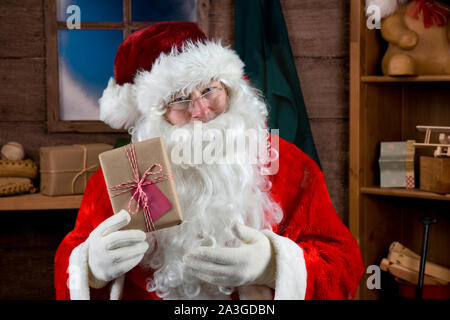 Santa mit plain wrapped Weihnachtsgeschenk in seiner Werkstatt Stockfoto