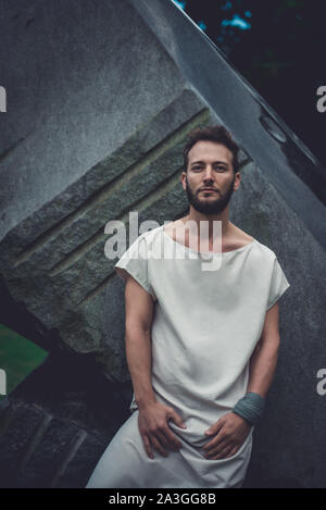 Ein mürrischer Porträt-Mann Mitte dreißig mit einem intensiven Blick, der sich auf eine große dunkle Steinstruktur lehnt. Stockfoto